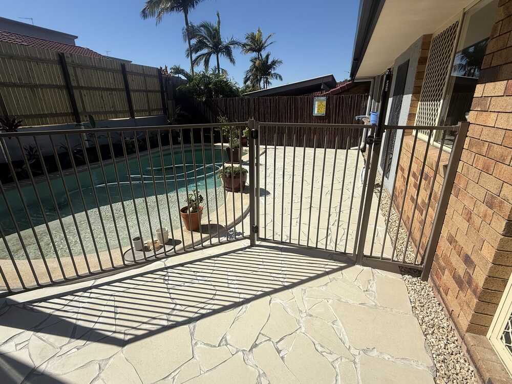 Bronze aluminium pool fence and gate on sandstone crazy paving beside a pool