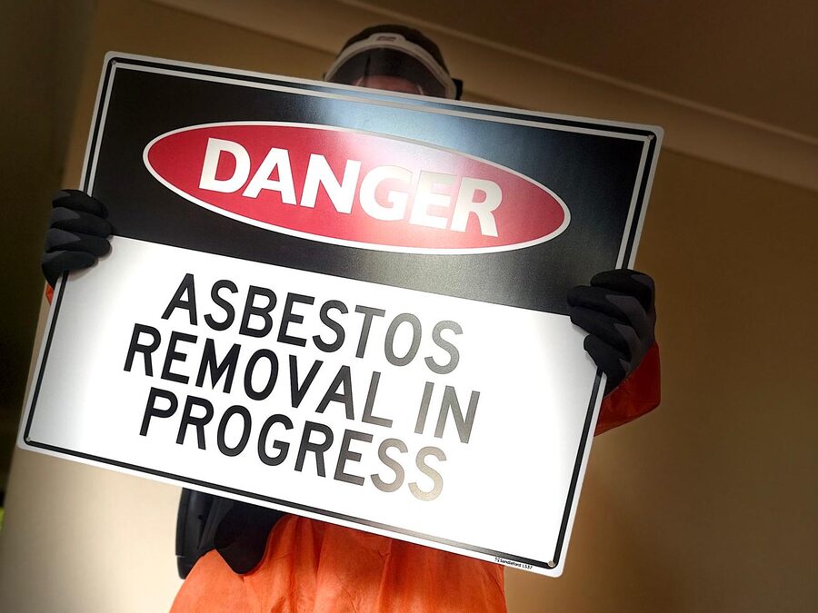 Licensed removalist in full protective equipment holding an asbestos removal warning sign