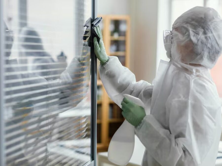 Technician in full protective equipment decontaminating a glass office partition